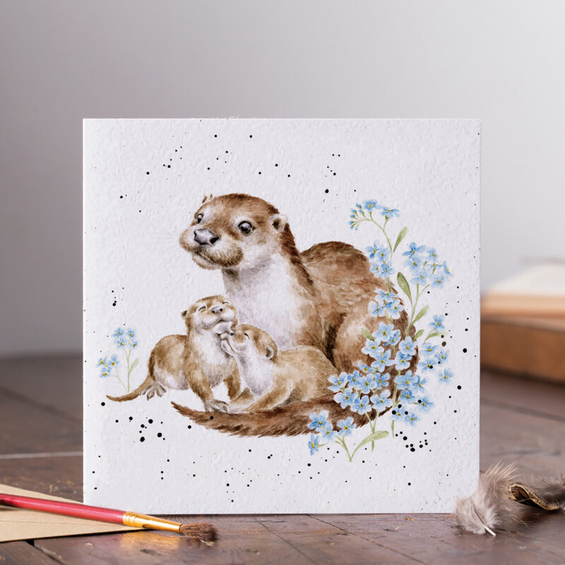 Glückwunschkarte auf weißem Hintergrund, bedruckt mit einer Otterfamilie und im Vordergrund blaue Blümchen