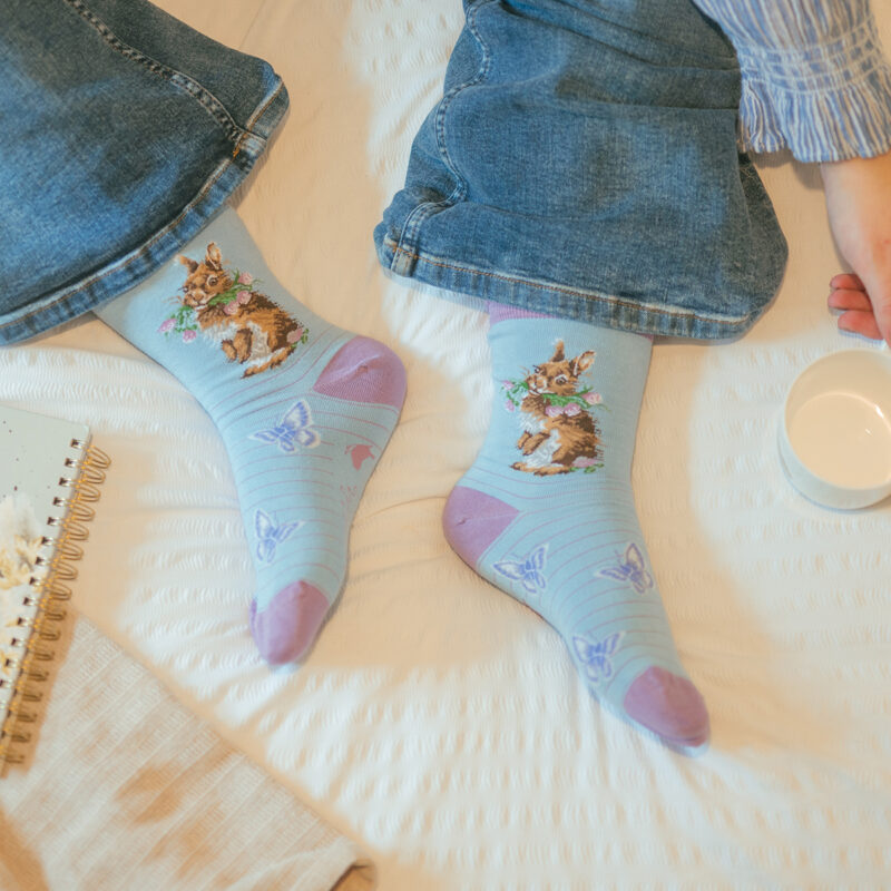 blau/lilafarbene Socken, bestickt mit einem Kaninchen das Blumen im Maul hat
