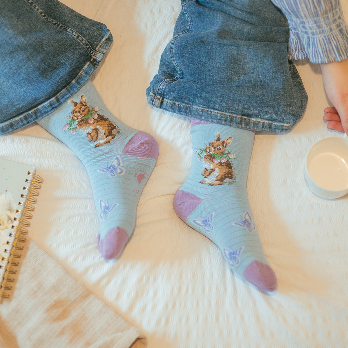 blau/lilafarbene Socken, bestickt mit einem Kaninchen das Blumen im Maul hat